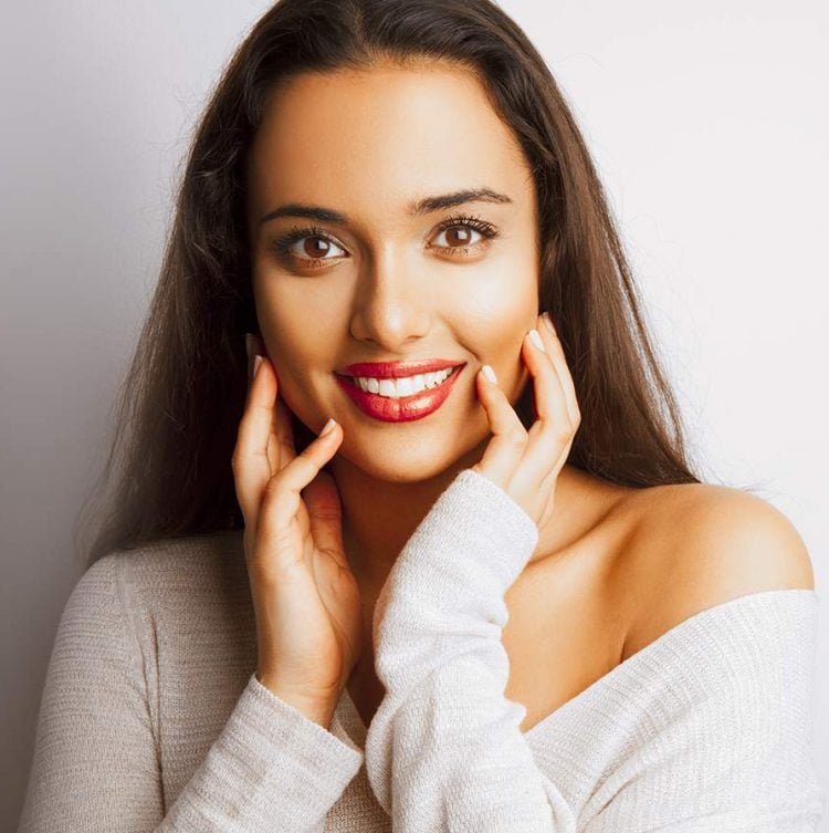 Menina sorrindo com as mãos perto do rosto 