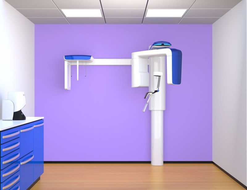 Dental imaging room featuring a panoramic X-ray machine against a purple wall with blue cabinetry.