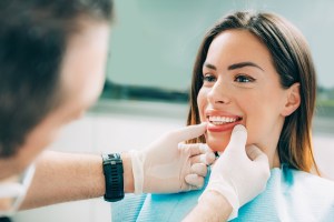 a woman smiles while a dentist touches her mouth